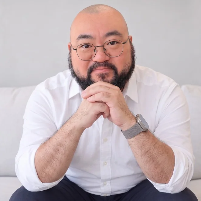 Jason Shew in a white shirt, sitting on a light grey sofa